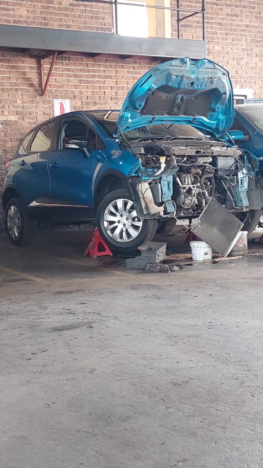 Blue hatchback on stands with the front end stripped for engine work